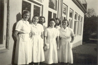 6 kvinnor i vita kläder framför byggnad

