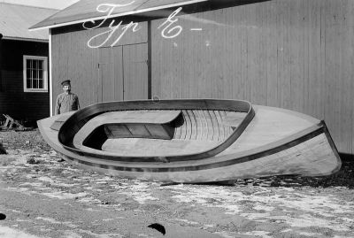 Man vid båt intill husvägg
Nyckelord: Båt