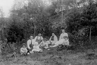 1 man 3 kvinnor och 4 barn sittande i skogsbacke
