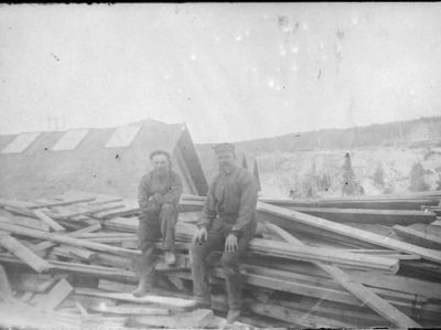 2 män sittande på brädhög
