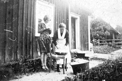 Två kvinnor vid tvättbaljor framför byggnad
Nyckelord: Tvättbalja