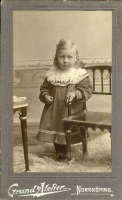 Liten flicka stående vid stol
