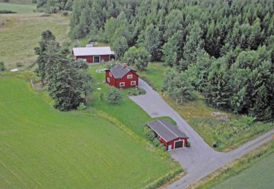 Flygbild över rödfärgat torp i skogsbryn
