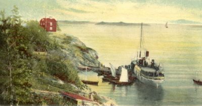 Ångbåt och segelbåtar vid brygga i skärgård
